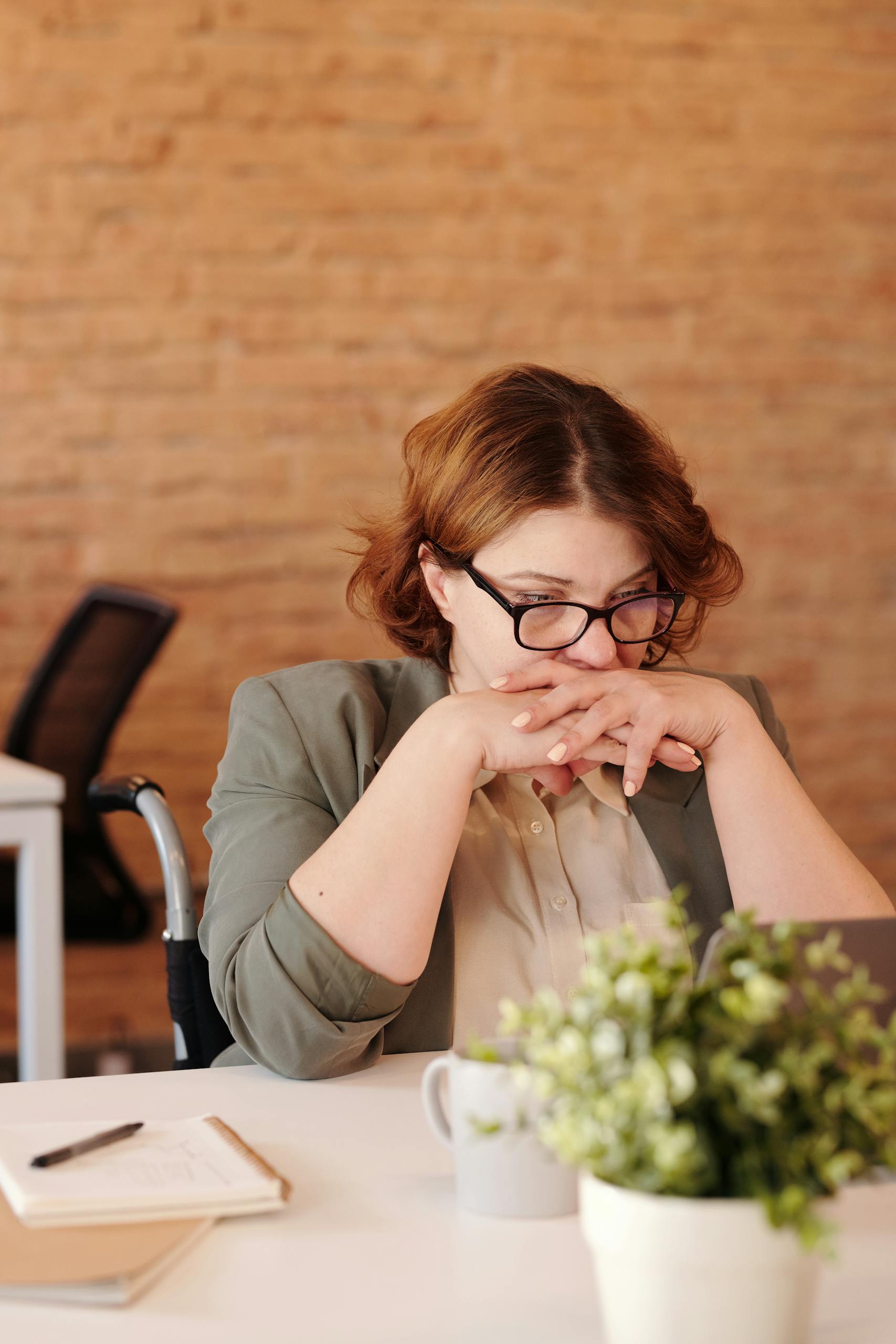 Female professional in wheelchair, deep in thought at home office desk.